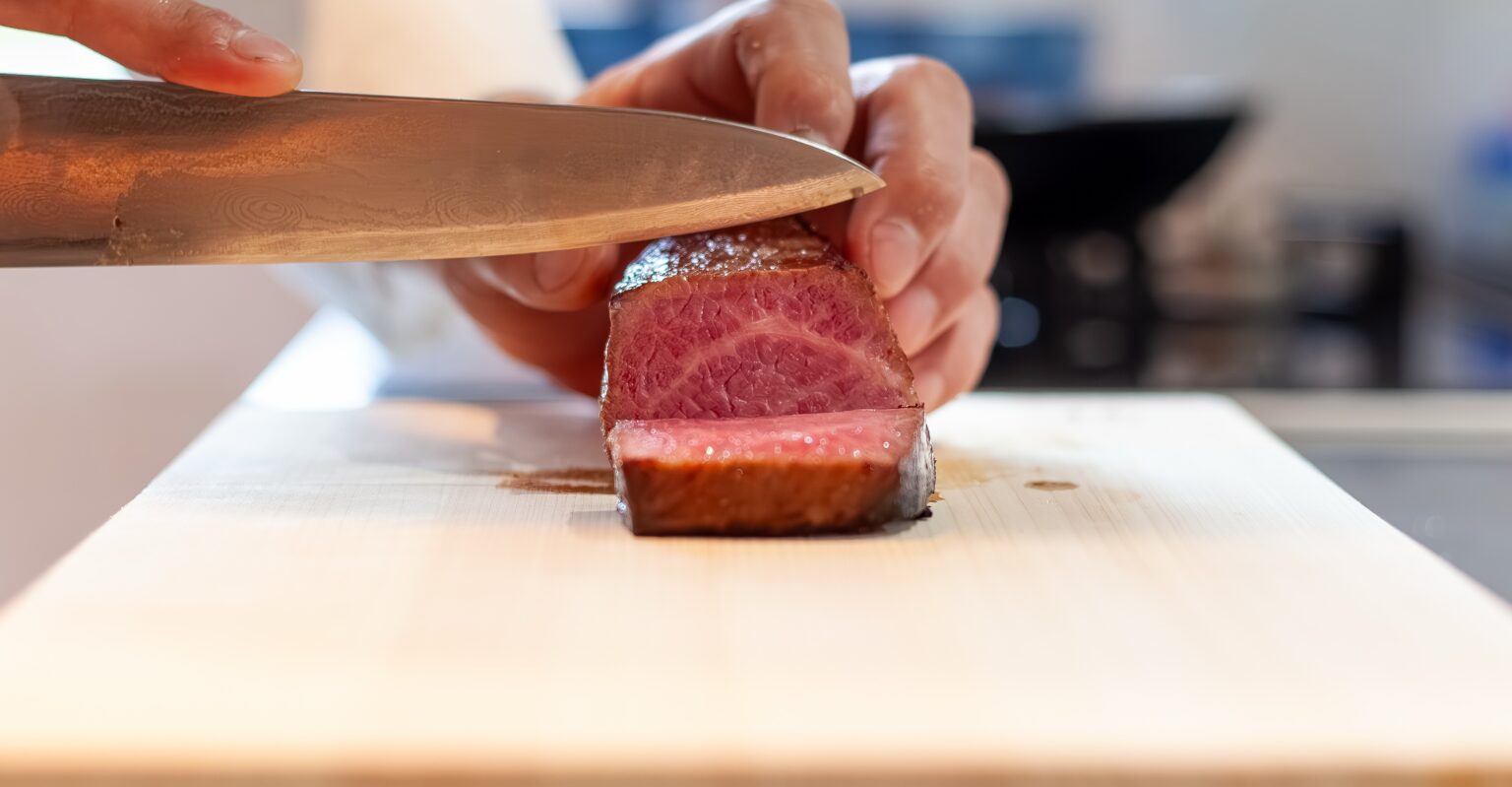 まな板の上で、火を入れた牛肉を包丁で切り分けているところ